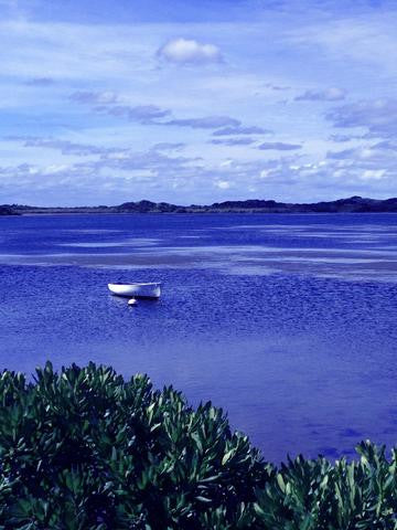 A blue still ocean with a row boat sitting there in the middle.