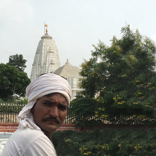 A man looking at you with a wrap on the head with a temple in the background