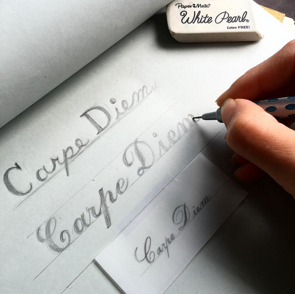 a hand writing out carpe diem in different fonts for engraving 