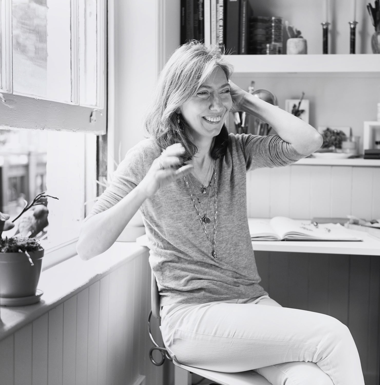 Bespoke Engagement Rings London. Meet Tarra Rosenbaum the Jeweller and designer of your bespoke jewellery. Photo is in black and white of Tarra in front of her desk at the window laughing. . 