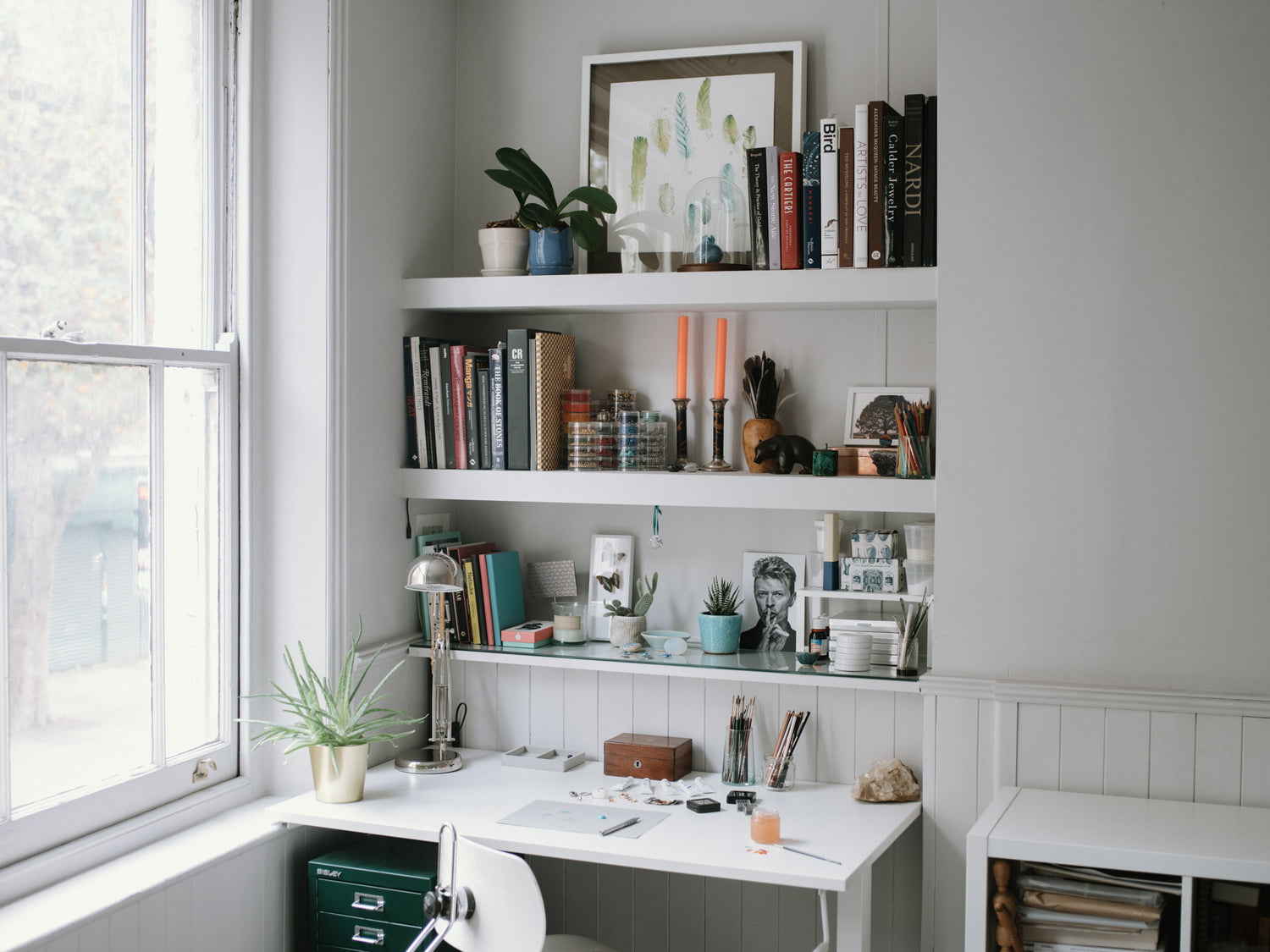 jewellery maker London, a look at one of the desks Tarra Rosenbaum does the designing and painting over her jewellery. There is a Bisley cabinet, orchids, painting and books lining the shelves. 